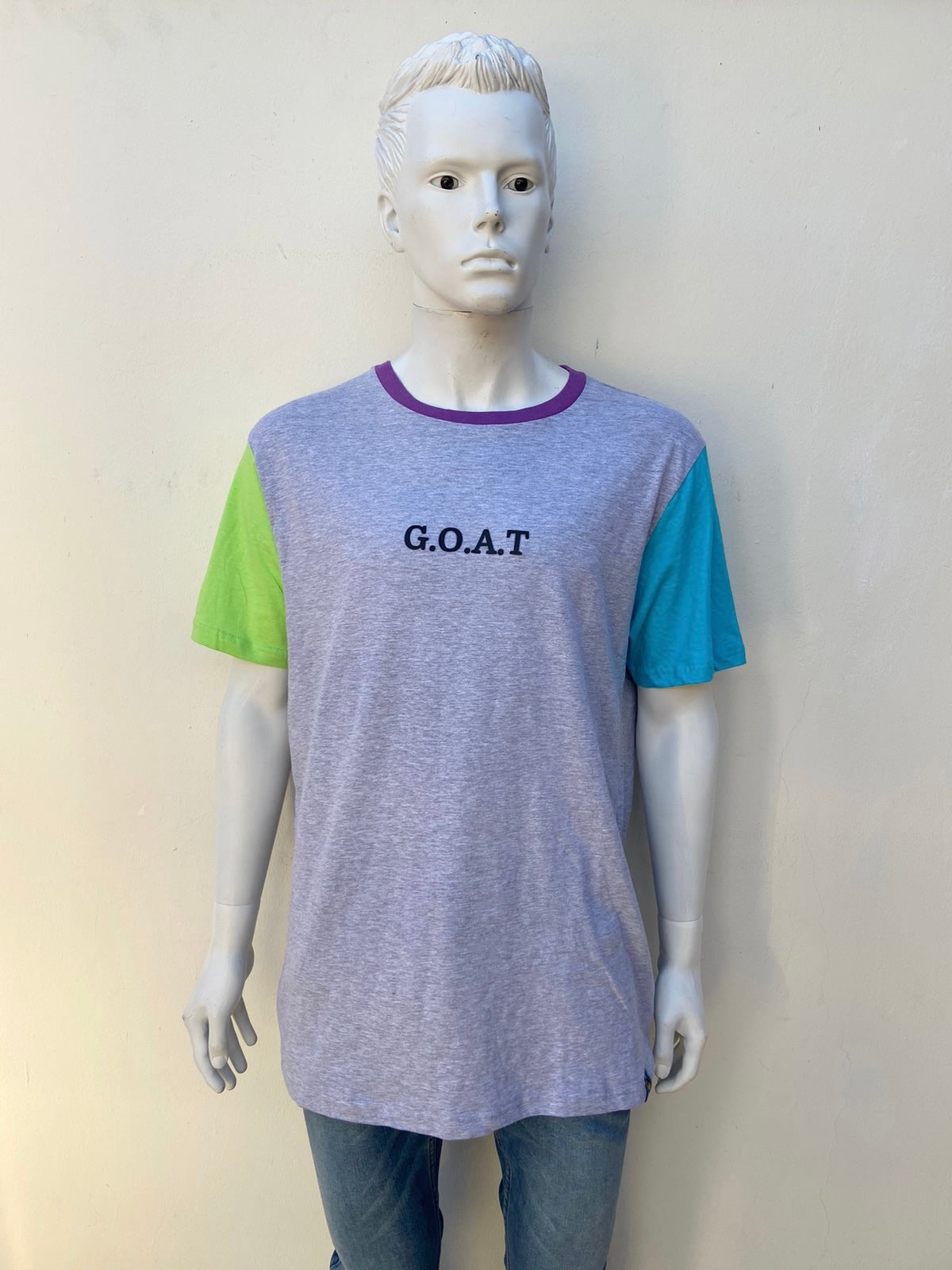 T-shirt W X Y Z original de color gris con manga derecha verde manga izquierda azul y cuello a color morado con letra G.O.A.T en negro al frente